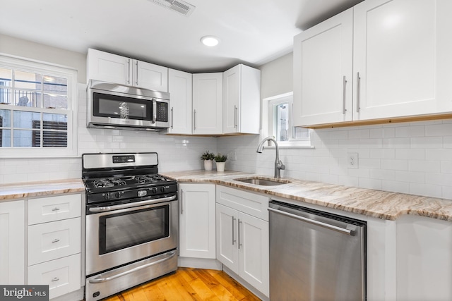 kitchen featuring appliances with stainless steel finishes, sink, white cabinetry, and light stone counters