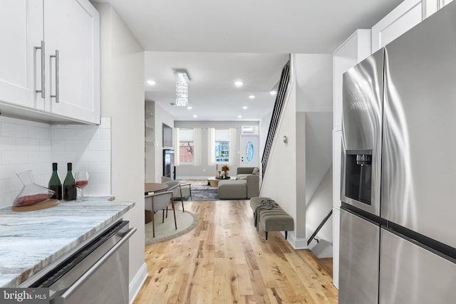 kitchen featuring stainless steel appliances, light stone counters, light hardwood / wood-style floors, backsplash, and white cabinetry