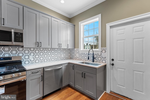 kitchen with sink, gray cabinetry, tasteful backsplash, ornamental molding, and stainless steel appliances