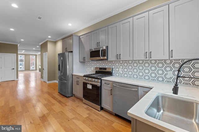 kitchen with light hardwood / wood-style flooring, ornamental molding, gray cabinets, stainless steel appliances, and decorative backsplash