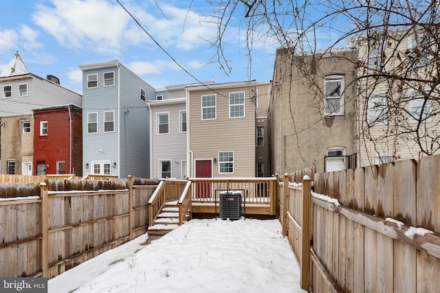 snow covered house with cooling unit and a wooden deck