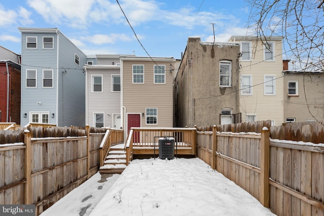 snow covered back of property with central air condition unit and a deck