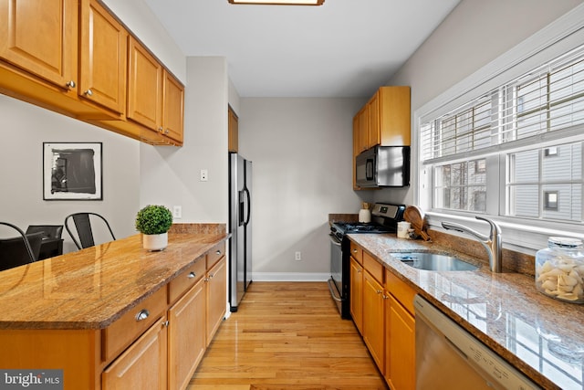 kitchen with light stone counters, sink, light hardwood / wood-style floors, and appliances with stainless steel finishes