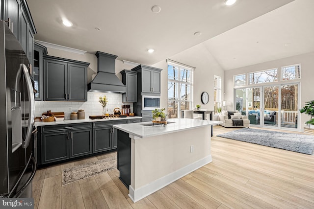 kitchen featuring stainless steel appliances, light countertops, light wood-style floors, open floor plan, and premium range hood