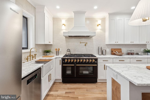 kitchen featuring premium range hood, appliances with stainless steel finishes, tasteful backsplash, white cabinets, and light hardwood / wood-style flooring