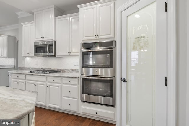 kitchen featuring white cabinetry, stainless steel appliances, crown molding, and backsplash