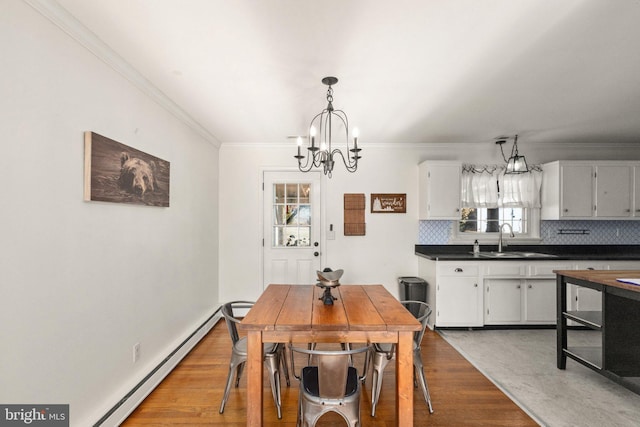 dining room featuring sink, baseboard heating, a notable chandelier, wood-type flooring, and ornamental molding