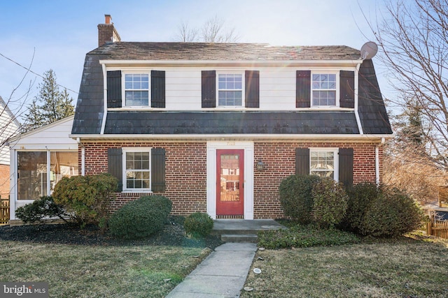 view of front of house featuring brick siding, a chimney, and a front lawn