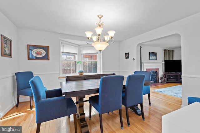 dining area with a brick fireplace, a chandelier, and light hardwood / wood-style flooring