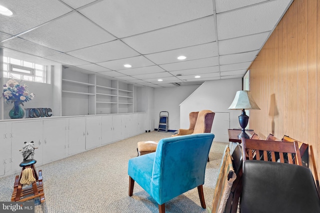 sitting room featuring a drop ceiling, built in shelves, and carpet flooring