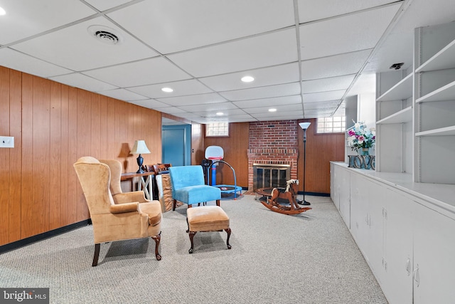 living area with light carpet, a fireplace, wooden walls, and a drop ceiling