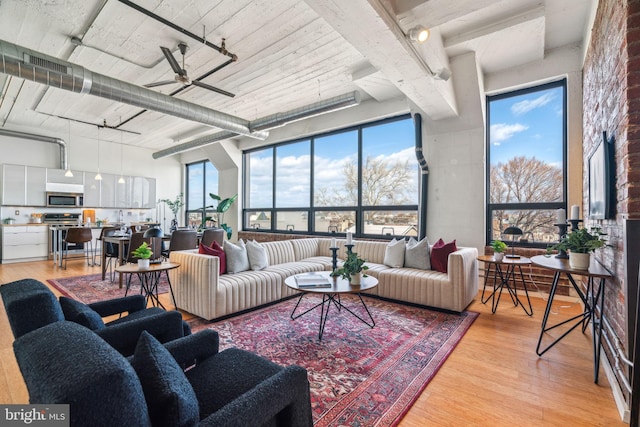 living room featuring ceiling fan, a towering ceiling, plenty of natural light, and light hardwood / wood-style flooring