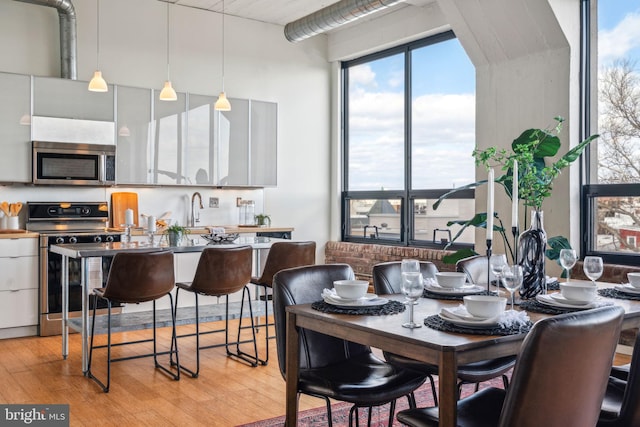 kitchen with white cabinetry, appliances with stainless steel finishes, light hardwood / wood-style floors, and decorative light fixtures