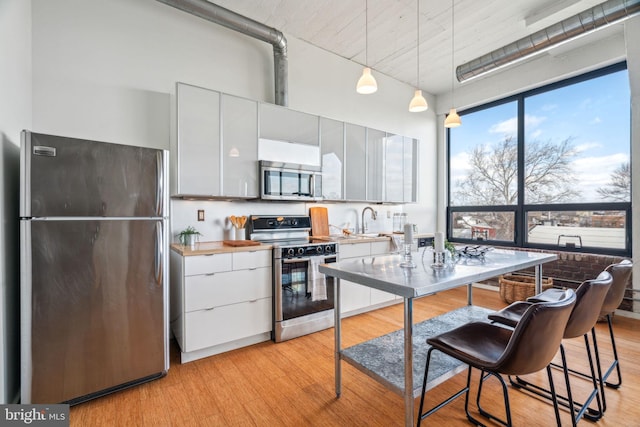 kitchen featuring sink, appliances with stainless steel finishes, hanging light fixtures, light hardwood / wood-style floors, and white cabinets