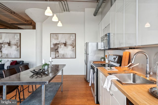 kitchen with sink, butcher block countertops, white cabinetry, hanging light fixtures, and stainless steel appliances