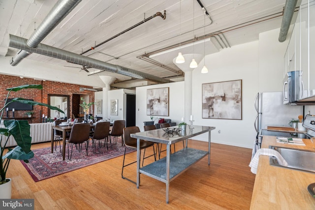 dining area with brick wall, sink, and light wood-type flooring