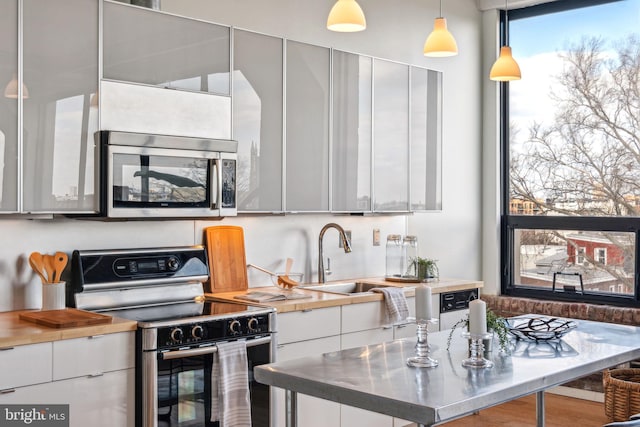 kitchen with white cabinetry, stainless steel appliances, sink, and hanging light fixtures