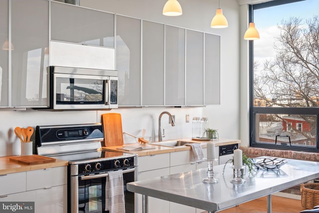 kitchen with appliances with stainless steel finishes, sink, pendant lighting, and white cabinets