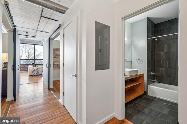 corridor with wood-type flooring, a barn door, and electric panel