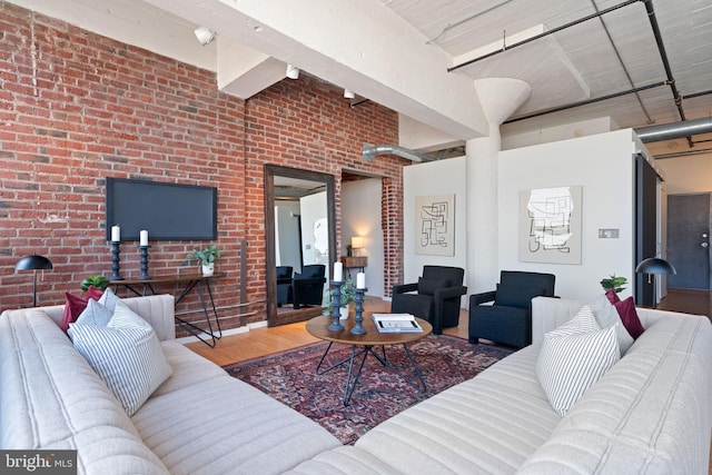 living room with hardwood / wood-style flooring, brick wall, and a towering ceiling