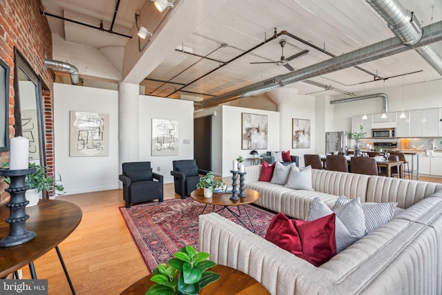 living room featuring a towering ceiling, light hardwood / wood-style floors, ceiling fan, and brick wall