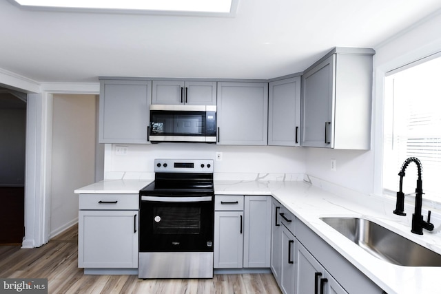 kitchen with light stone counters, light wood finished floors, gray cabinets, a sink, and appliances with stainless steel finishes