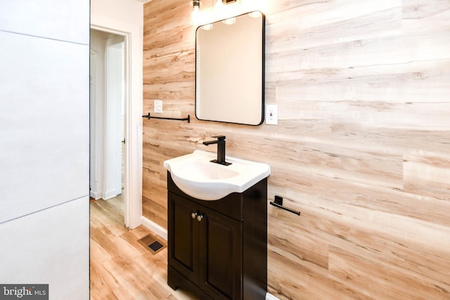 bathroom with visible vents, wood walls, vanity, and wood finished floors
