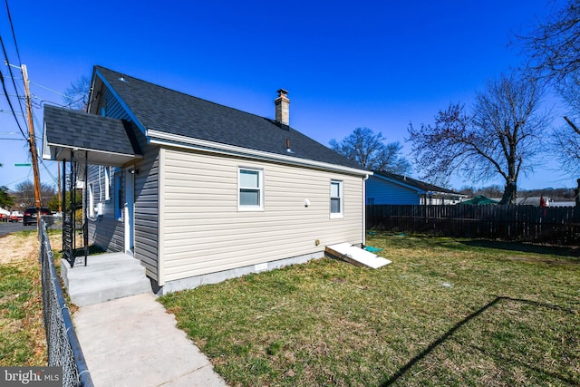 rear view of house with a shingled roof, a chimney, a yard, and fence