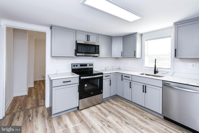 kitchen with a sink, appliances with stainless steel finishes, gray cabinets, and light countertops