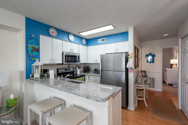 kitchen featuring a peninsula, light stone countertops, visible vents, and stainless steel appliances