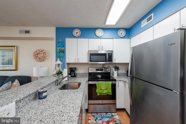 kitchen featuring light stone counters, a sink, visible vents, white cabinetry, and appliances with stainless steel finishes