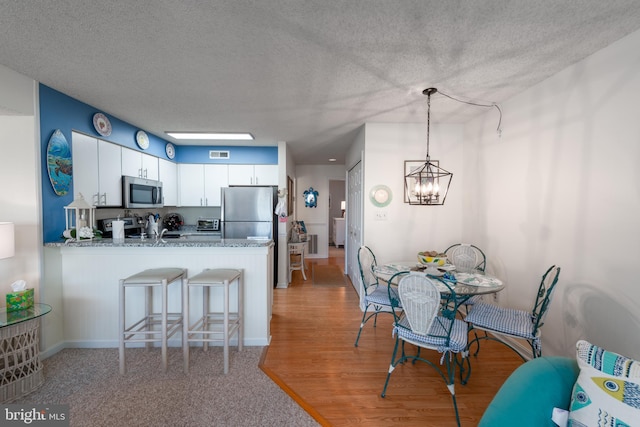 kitchen featuring a textured ceiling, stainless steel appliances, a peninsula, white cabinets, and light wood-type flooring