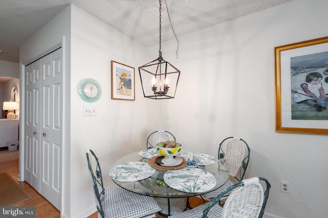 dining area featuring an inviting chandelier, baseboards, a textured ceiling, and wood finished floors