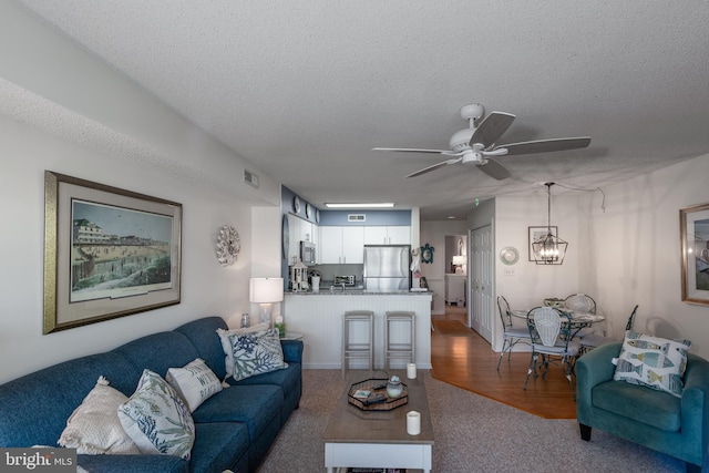 living area featuring visible vents, a textured ceiling, and ceiling fan with notable chandelier