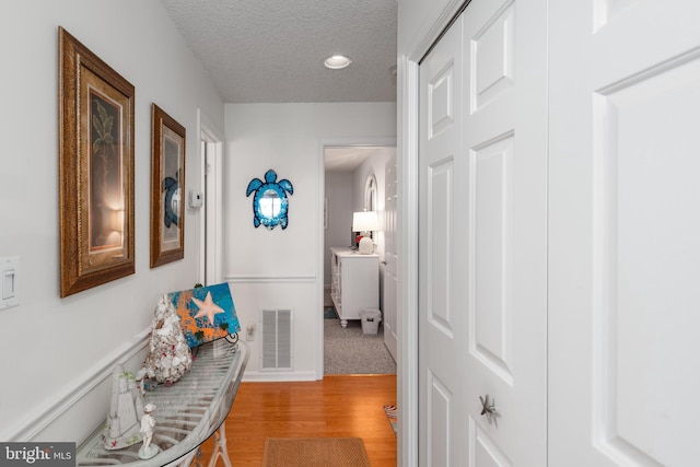 hallway with a textured ceiling, light wood-type flooring, visible vents, and recessed lighting