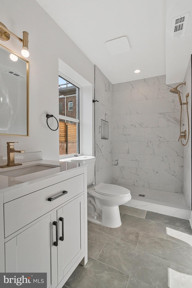 bathroom with vanity, tiled shower, and toilet