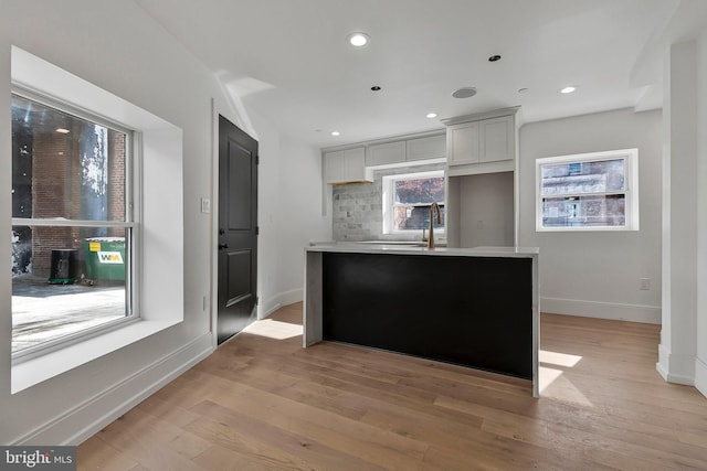 kitchen with decorative backsplash, a kitchen island, gray cabinets, and light wood-type flooring