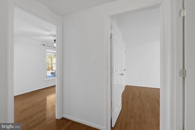 hallway featuring wood finished floors, baseboards, and a textured ceiling