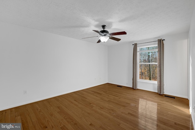 spare room featuring visible vents, baseboards, a textured ceiling, and wood finished floors