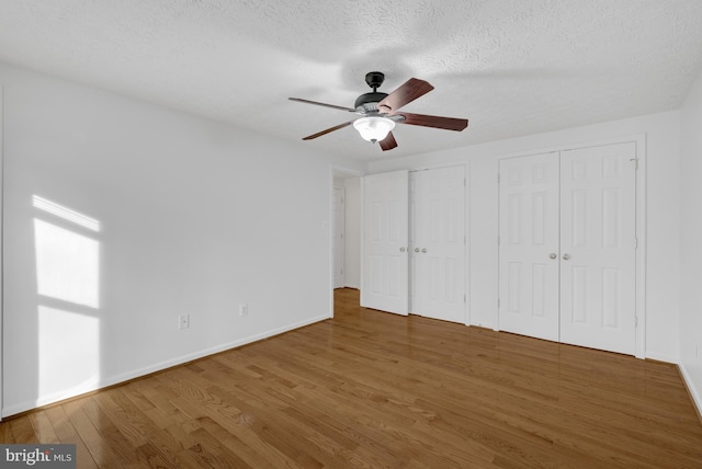 unfurnished bedroom with baseboards, two closets, wood finished floors, and a textured ceiling