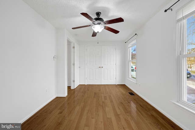 unfurnished bedroom featuring a textured ceiling, wood finished floors, visible vents, and baseboards