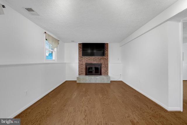 unfurnished living room featuring visible vents, a textured ceiling, wood finished floors, baseboards, and a brick fireplace