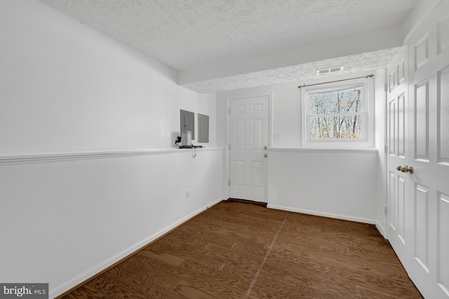 spare room featuring visible vents, electric panel, a textured ceiling, dark wood finished floors, and baseboards