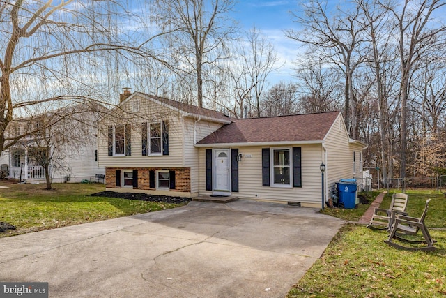 split level home with brick siding, a shingled roof, fence, a front yard, and a chimney