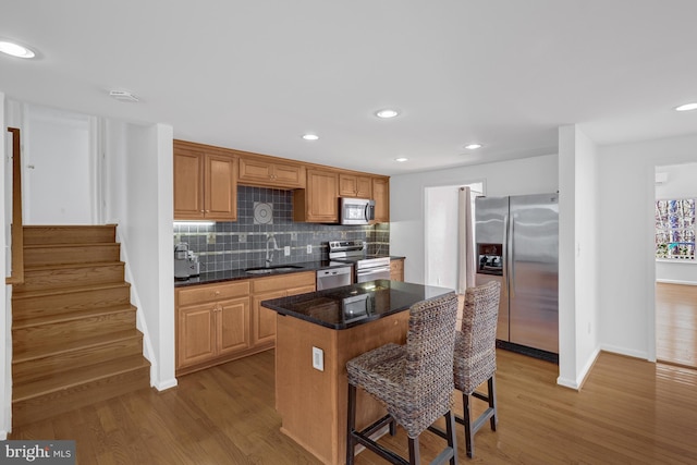 kitchen featuring light wood-style flooring, a sink, a kitchen breakfast bar, backsplash, and stainless steel appliances