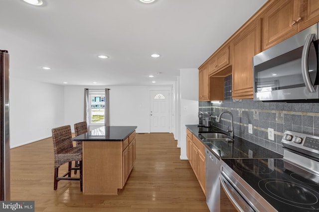 kitchen featuring a kitchen breakfast bar, stainless steel appliances, light wood-style floors, and a sink