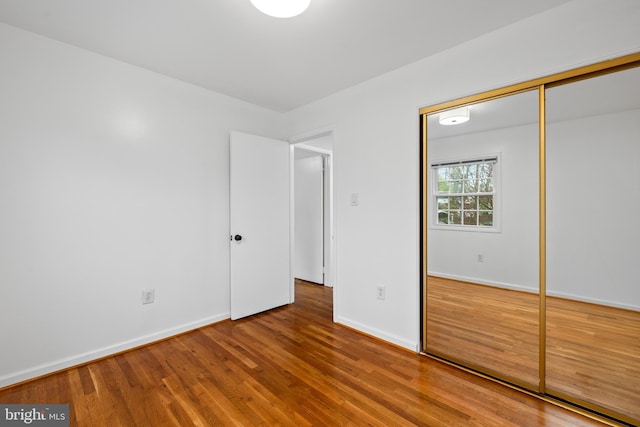 unfurnished bedroom with wood finished floors, baseboards, and a closet