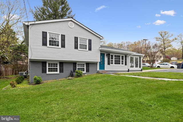 tri-level home featuring brick siding, central air condition unit, fence, and a front lawn