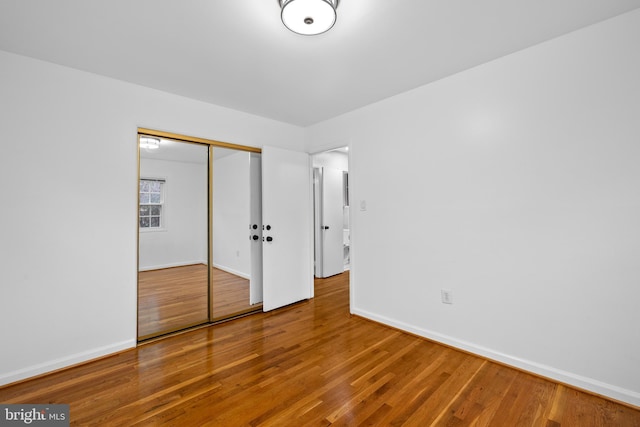 unfurnished bedroom featuring wood finished floors, a closet, and baseboards