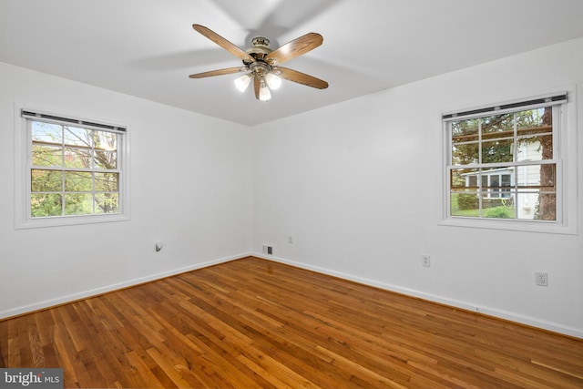 empty room featuring a wealth of natural light, ceiling fan, hardwood / wood-style floors, and baseboards